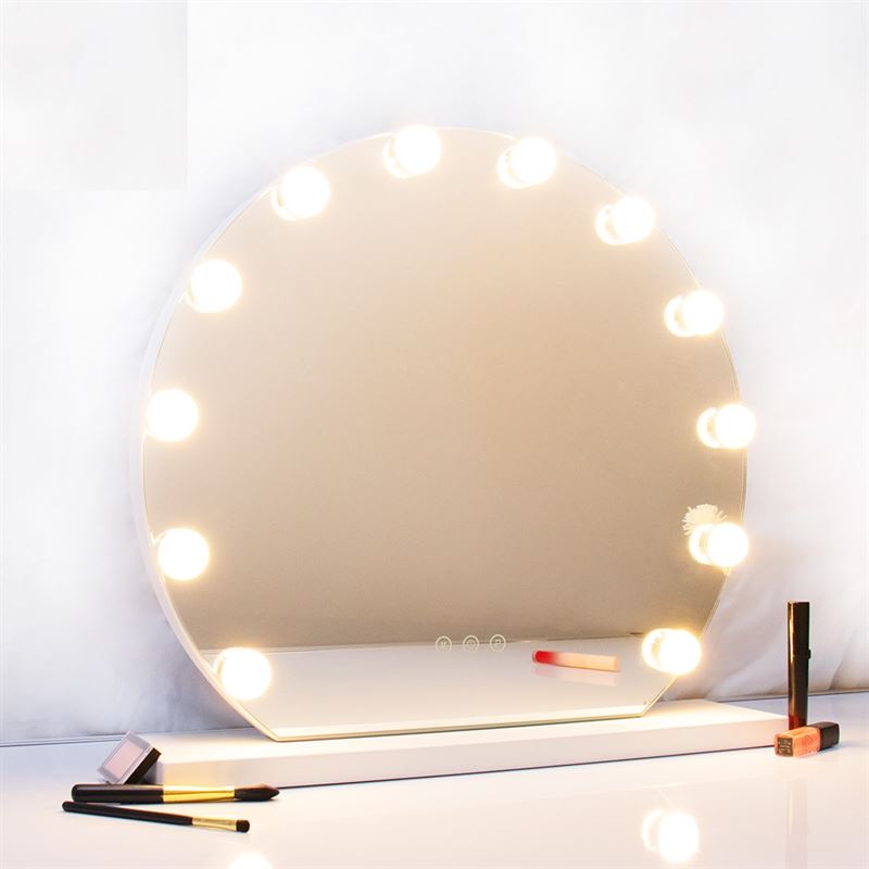 The UNIQ London Round Make-up Mirror by UNIQ, featuring 12 LED bulbs and a touch function in white, sits on a white surface, surrounded by makeup items such as brushes, lipstick, and mascara while reflecting a soft, neutral background.